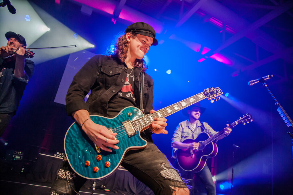 A man plays a blue electric guitar on stage.