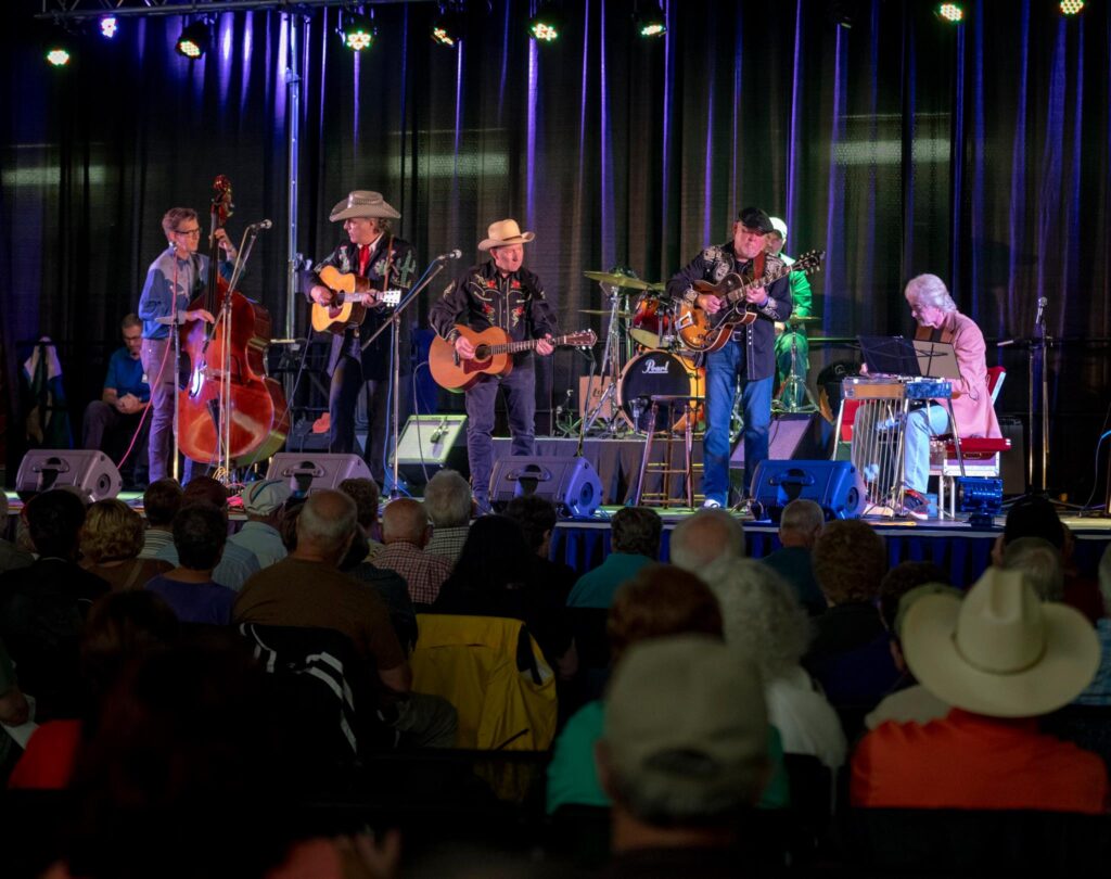A country music band plays on stage, many of the members wear cowboy hats.