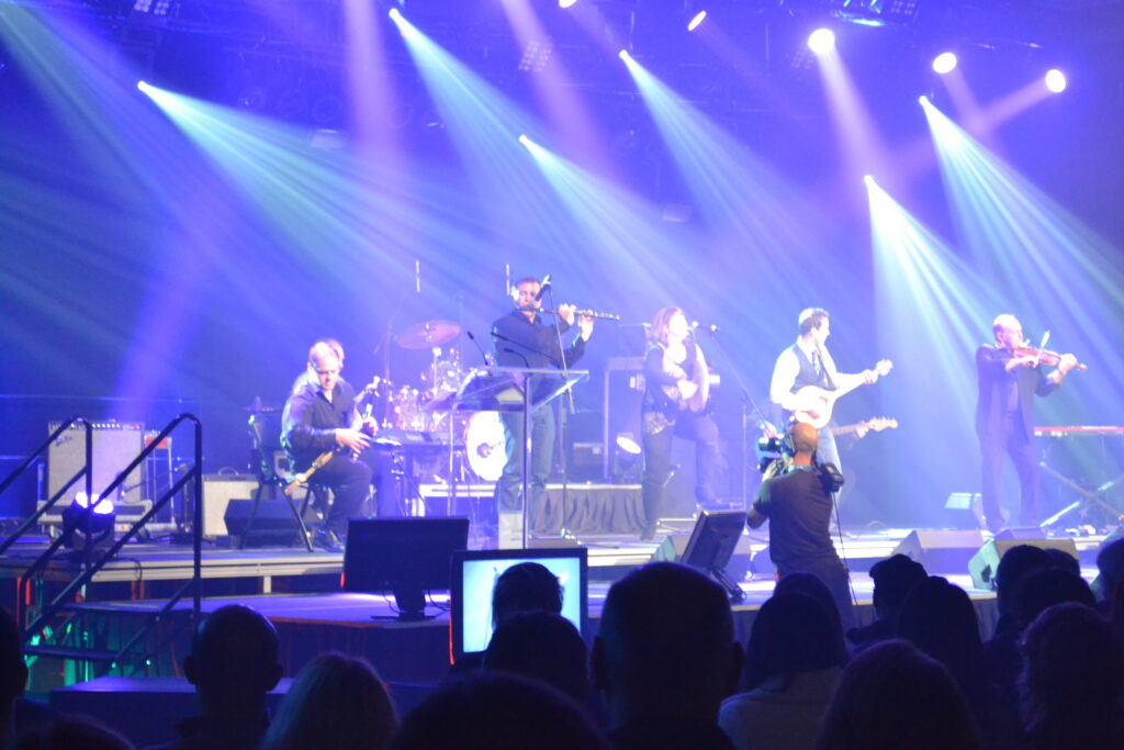 A band plays on a stage with bright lights above them.