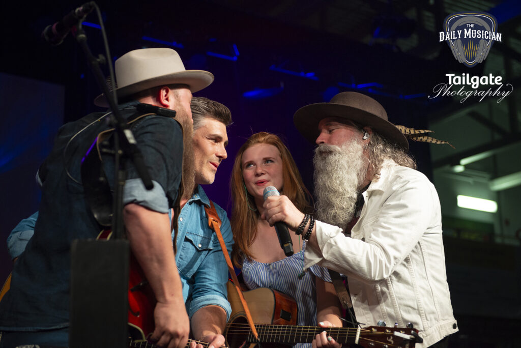 Three men and one woman sing into a microphone.